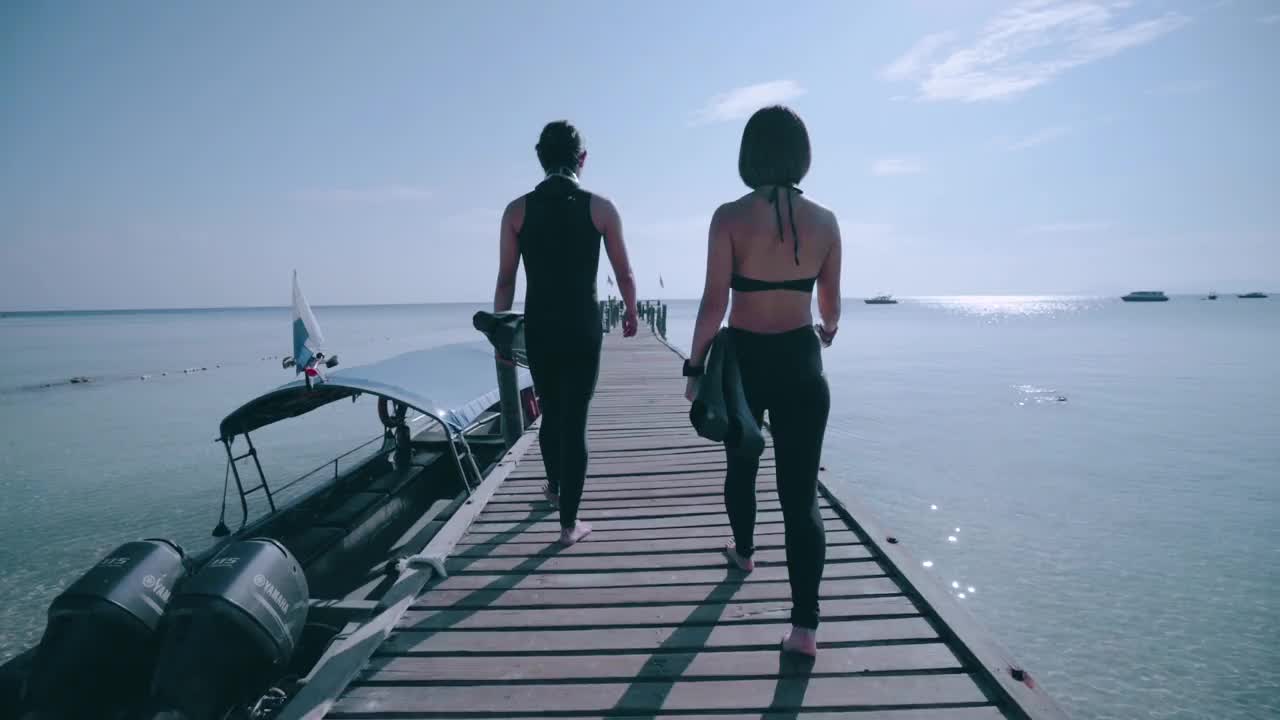 两名自由潜水员在木码头上走向大海的后视图视频素材