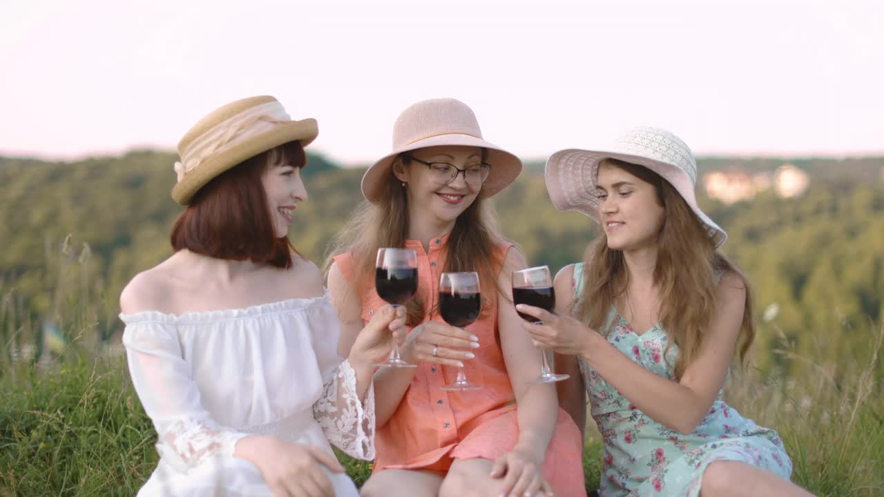 三个年轻的妇女戴着帽子和衣服，享受美味的食物，在夏季庆祝野餐视频下载