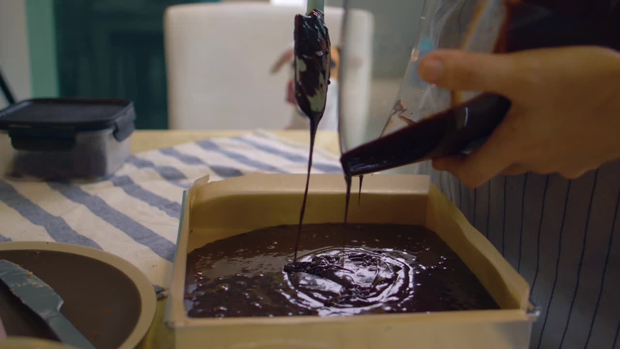 亚洲妇女把融化的巧克力倒在金属托盘做布朗尼咖啡视频素材