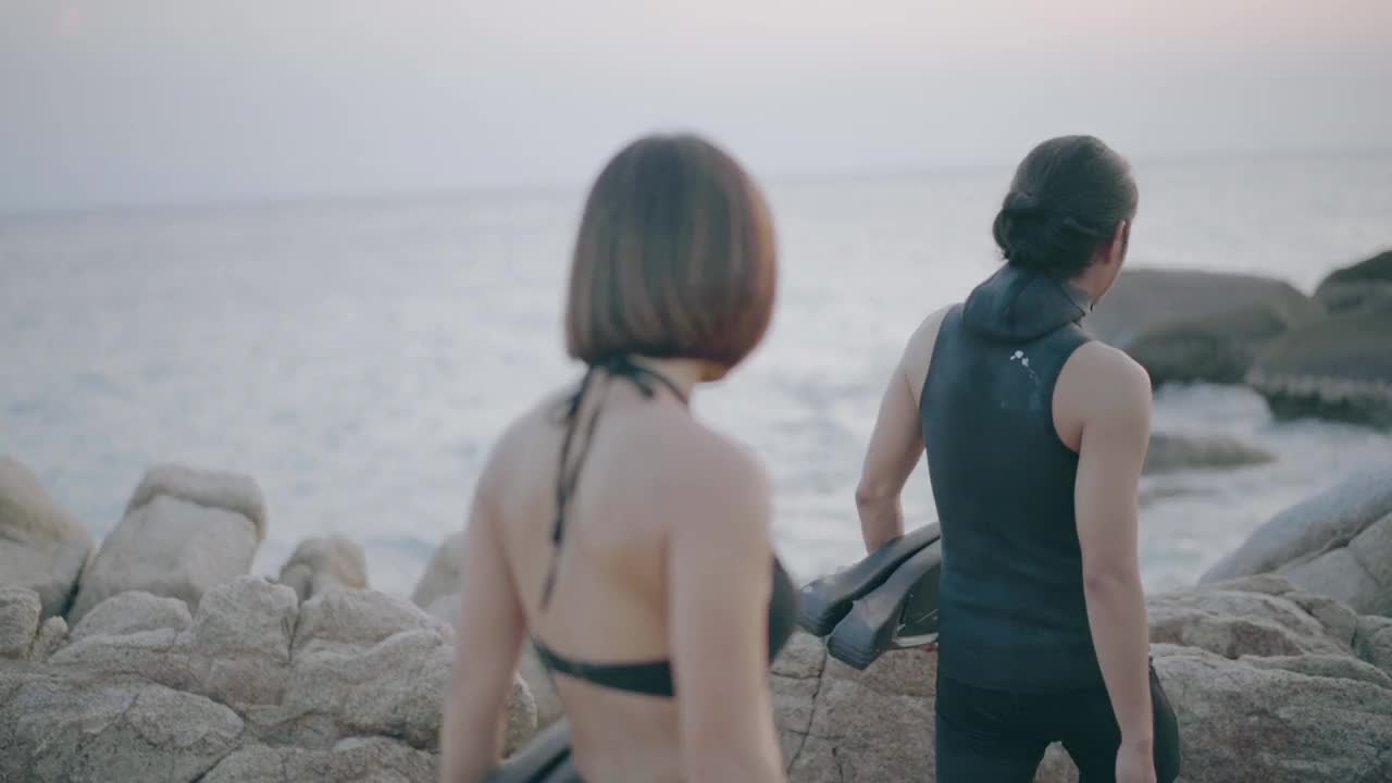 两个穿着泳衣和潜水服的人在海滩上与巨大的岩石交谈视频素材