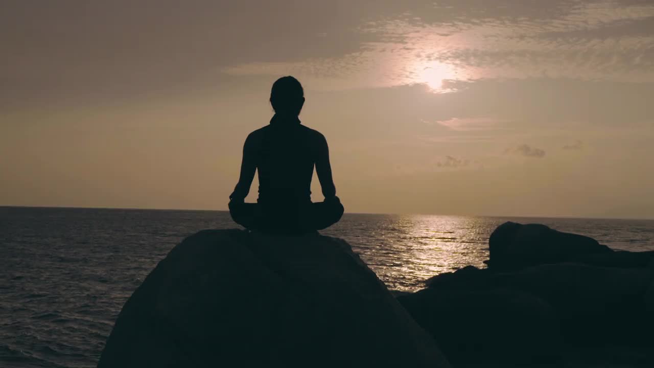 日落时分，一个人坐在面朝大海的岩石上做瑜伽视频下载