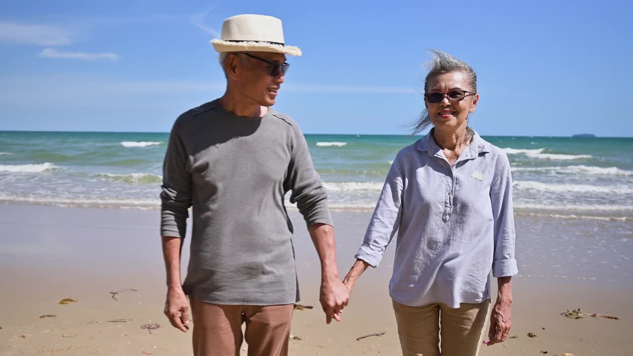 亚洲老年夫妇游客手牵手，在海滨沙滩上聊天在暑假。视频下载