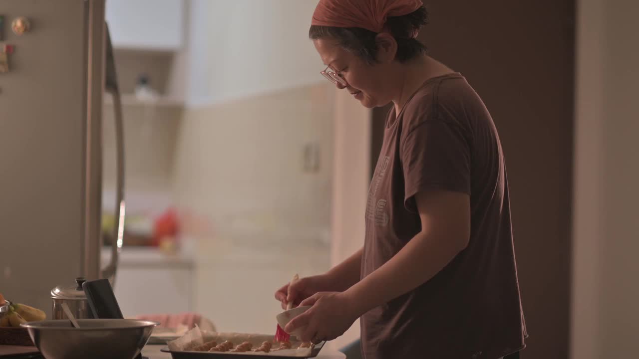 亚洲华人中年妇女戴着头巾在厨房的花生饼干上刷蛋黄视频下载