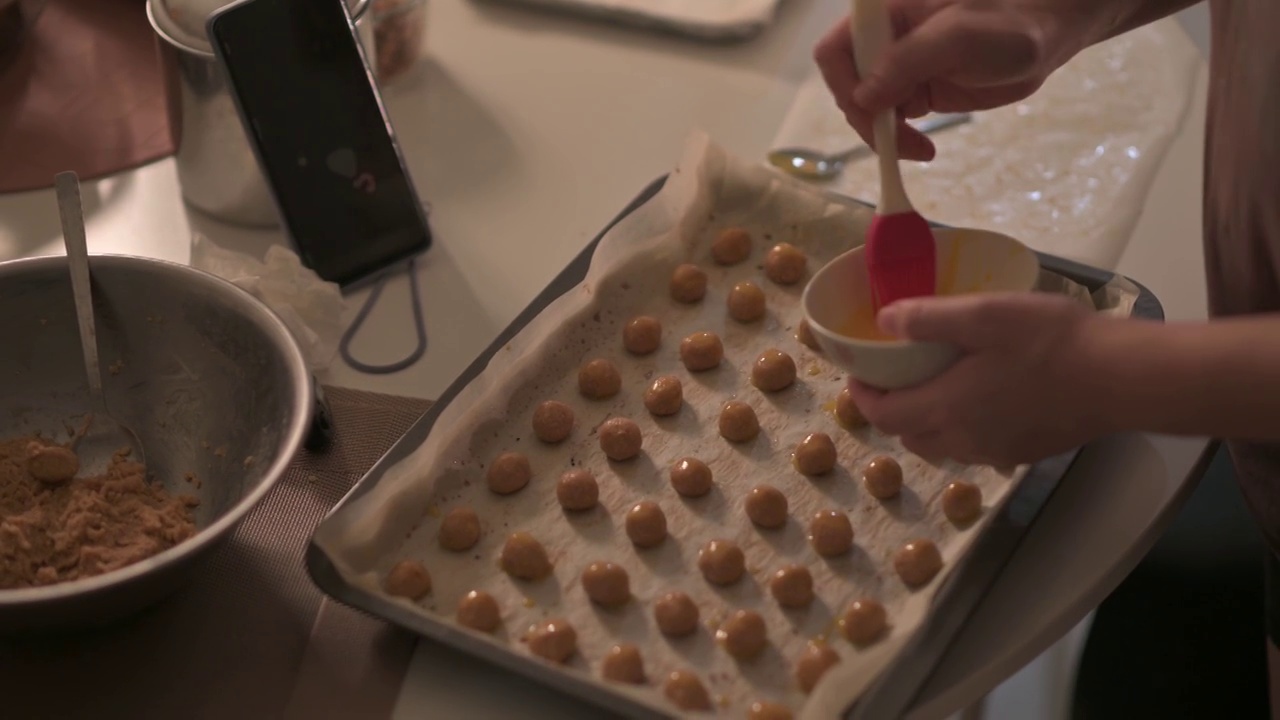 上角亚洲华人中年妇女在厨房的烤盘上用手把蛋黄涂在花生饼干饼干上视频素材