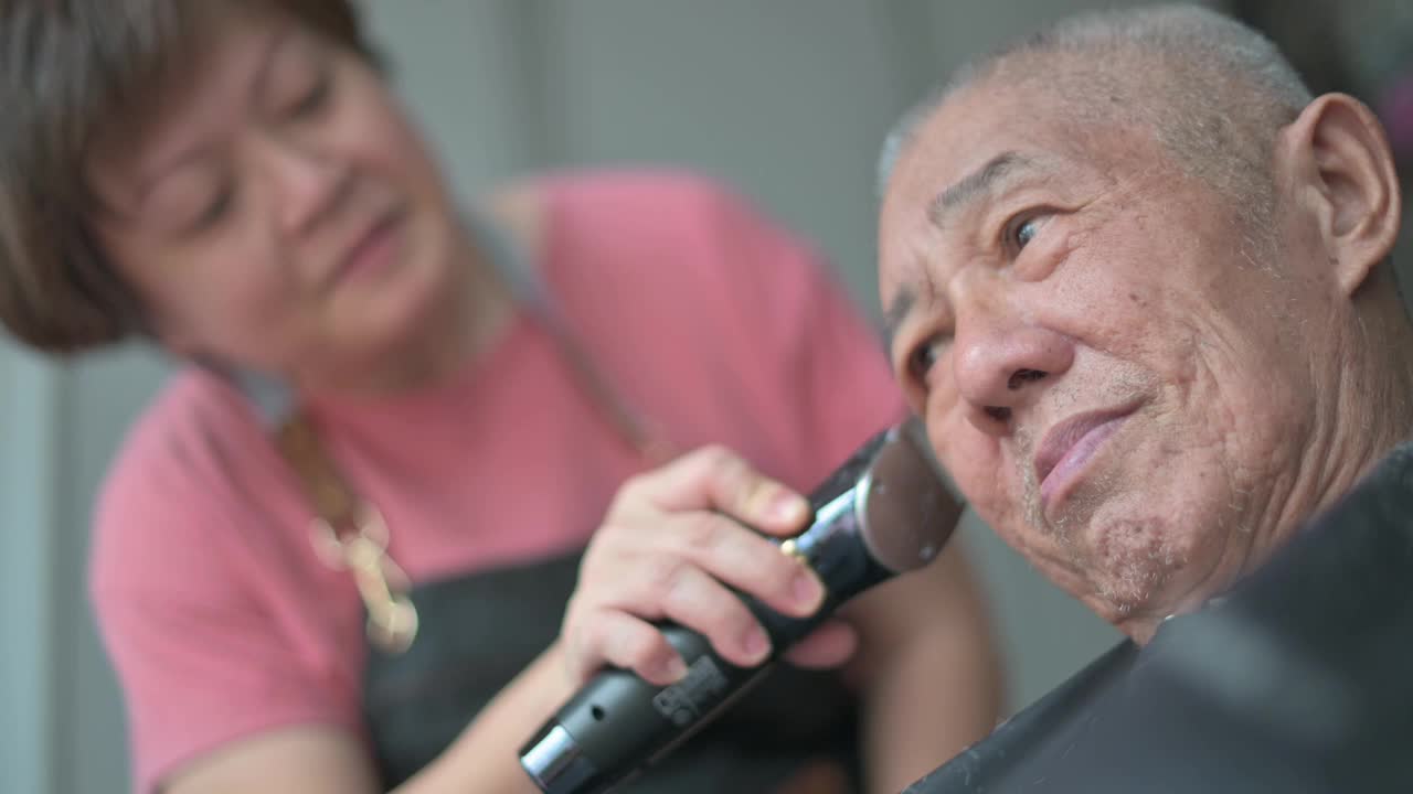 一名亚洲华人女子在白天坐在轮椅上为父亲理发视频下载