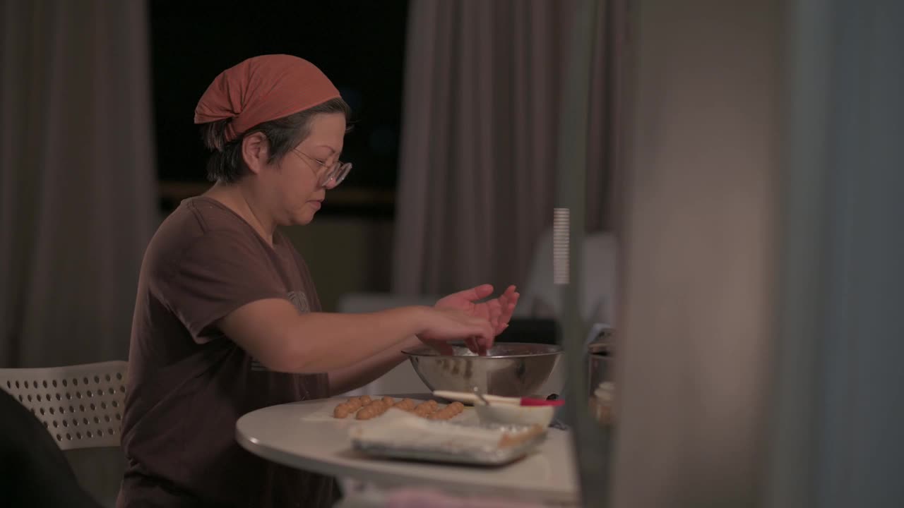 亚洲华人中成年妇女在家里的厨房里双手将花生饼干面团压在手掌上成型视频素材
