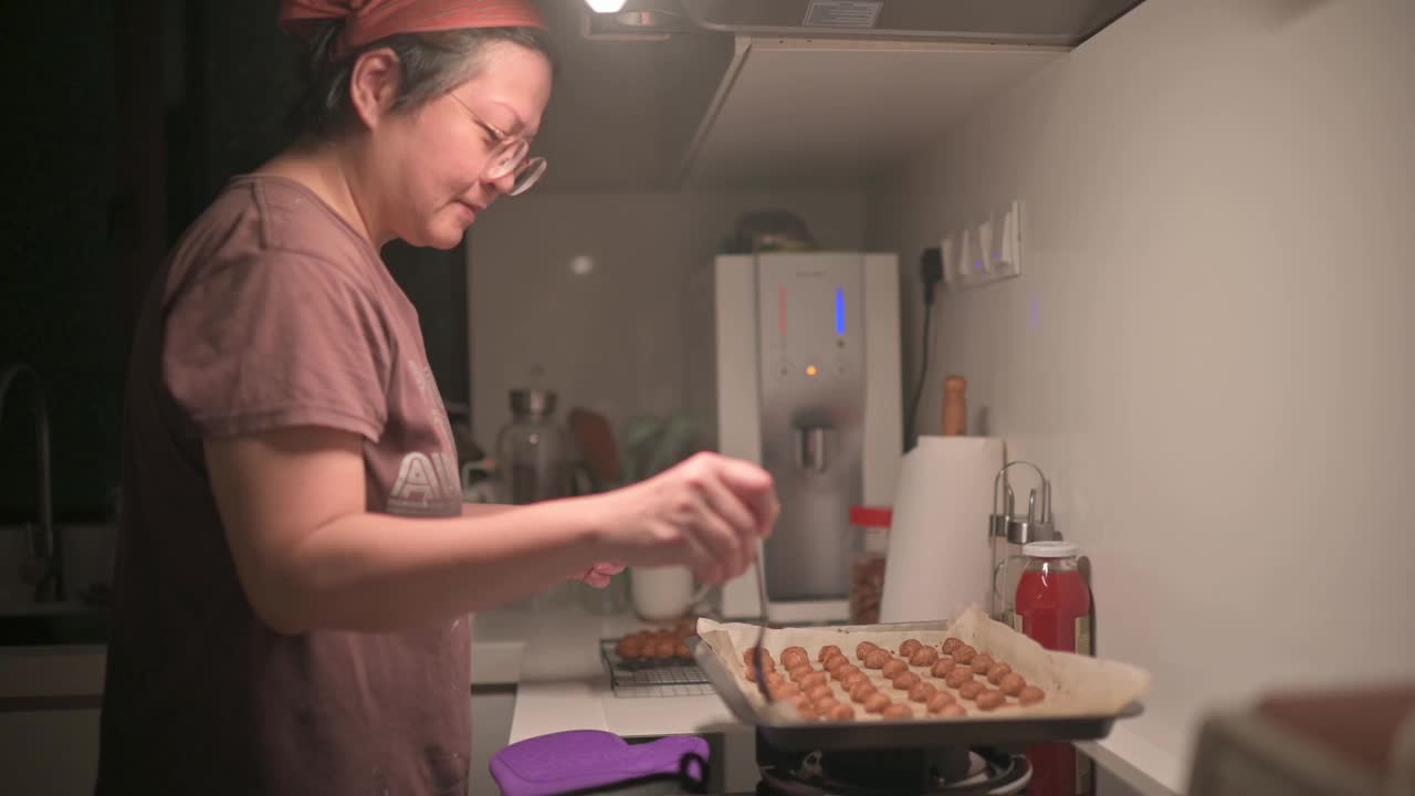 亚洲华人中年妇女在厨房拿起烤花生饼干视频素材