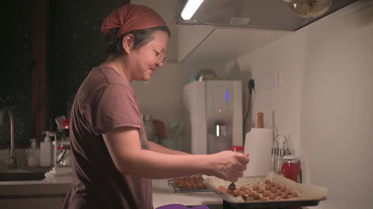 亚洲华人中年妇女在厨房拿起烤花生饼干视频素材