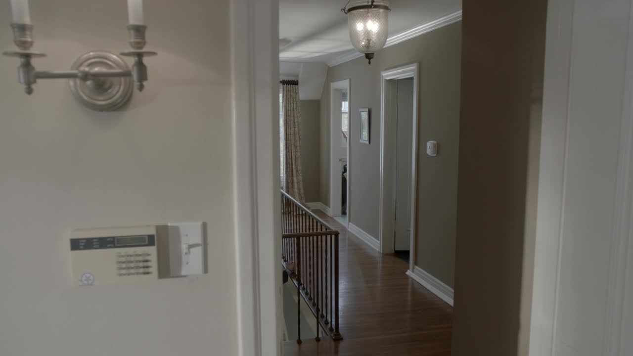 上层或中产阶级住宅楼上走廊的中等角度。墙壁壁灯，楼梯扶手和报警系统面板可见。视频素材