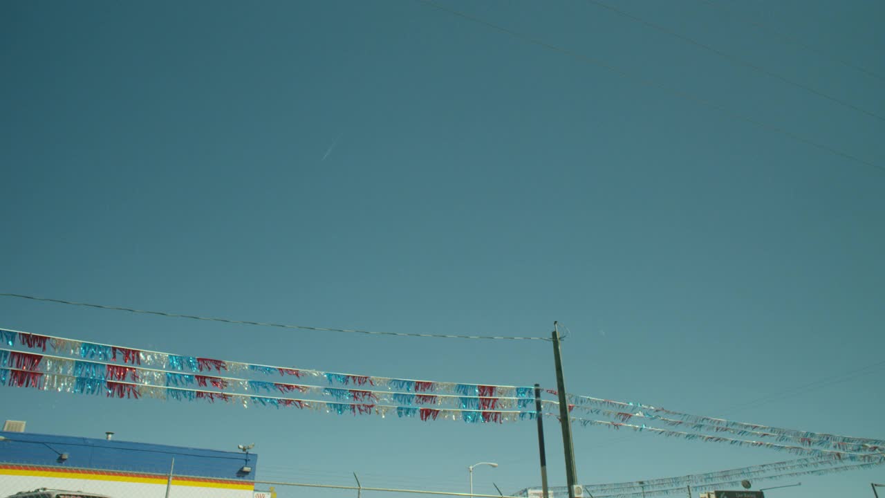 银色，蓝色和红色的飘带。可能是停车场。可能是二手车。电线杆可见。建筑部分可见。顶部的带刺铁丝网部分可见。视频下载