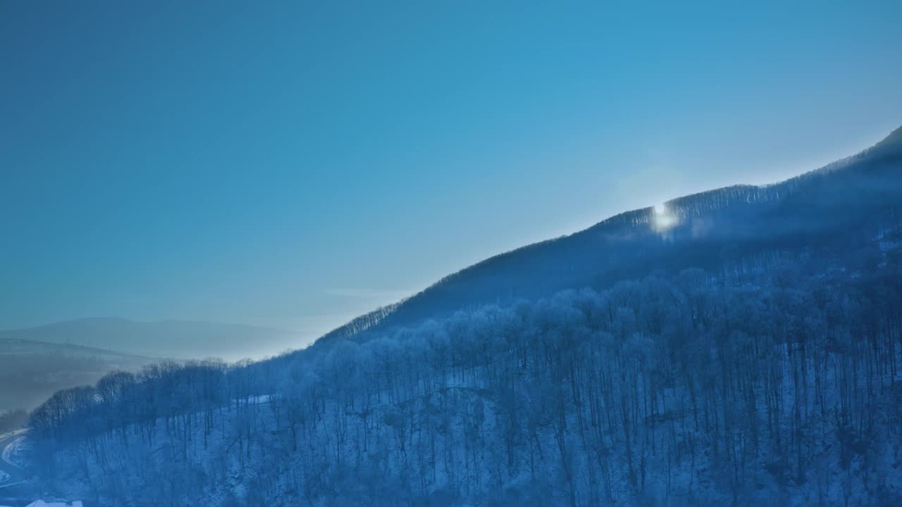 一架四轴飞行器在黎明拍摄的白雪覆盖的山地森林的美丽的冬季全景。视频素材