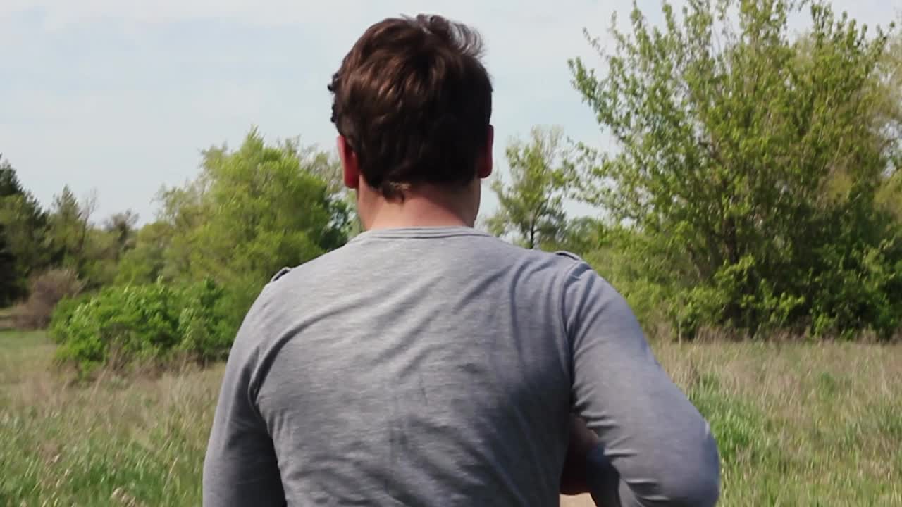 一个穿着轻便运动服的白人青年在一个绿色的公园里跑步视频下载