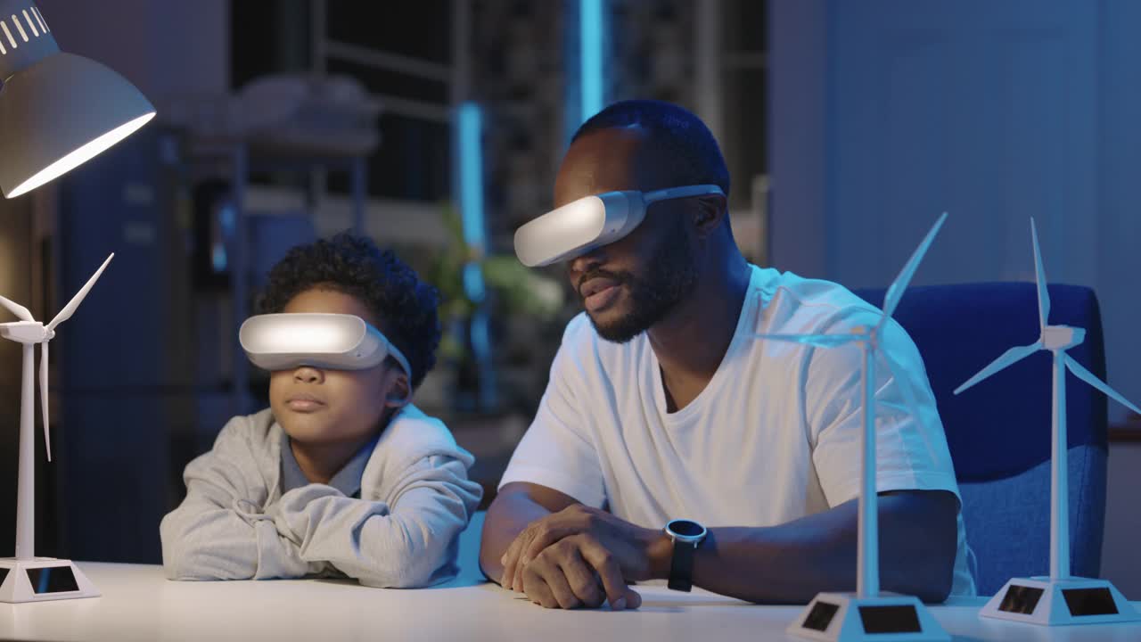 非洲家庭的父亲和9岁的儿子戴着虚拟现实耳机，晚上在家里一起讲授生态学和讨论解释替代能源模型涡轮机。创新的概念。视频素材