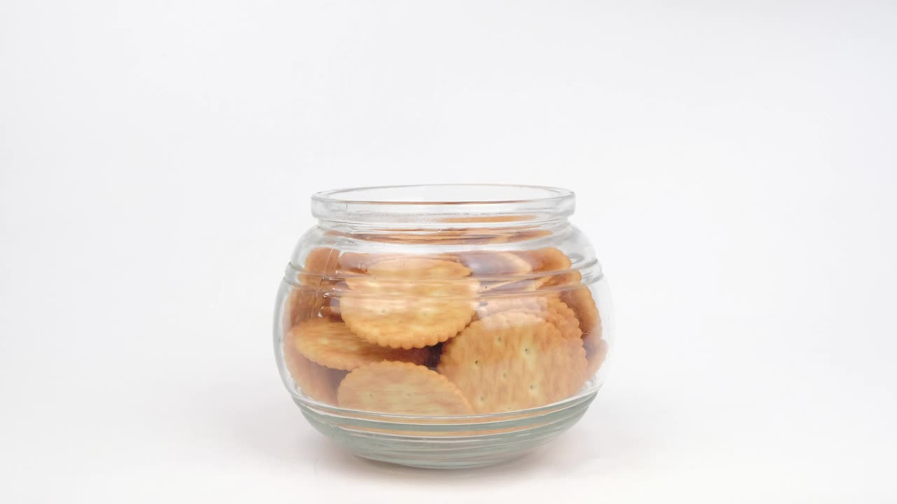手工挑选饼干饼干装在白色背景的玻璃罐中。视频下载