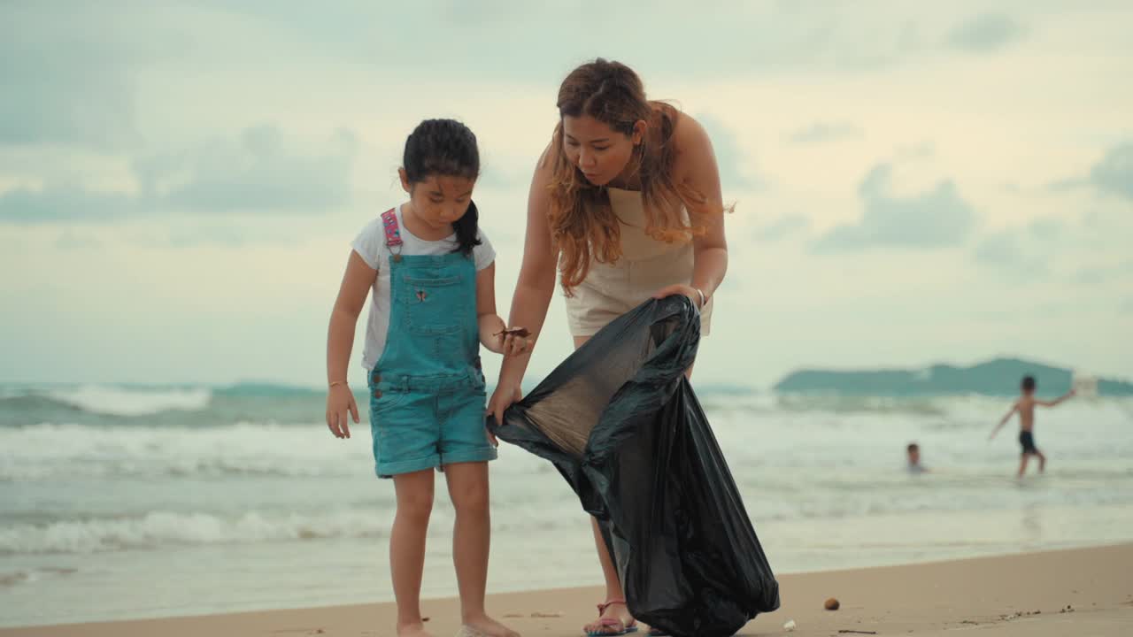 女儿和妈妈正享受夏日的海滩假期。小女孩在海滩上发现了一些垃圾，他们正在把它们捡起来视频下载