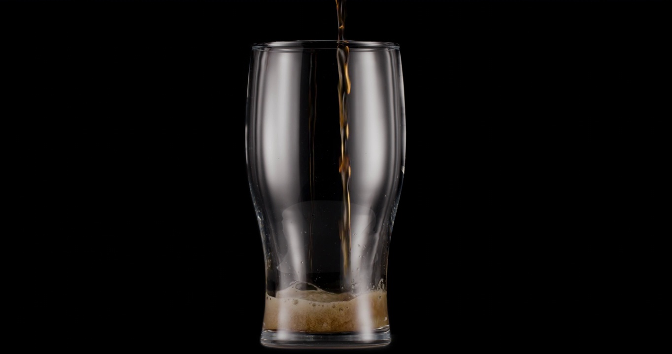 一杯黑色背景的黑啤酒。喷射机慢慢地将啤酒杯装满，造成大量的气泡和泡沫。视频素材