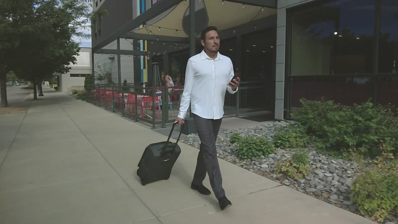 成年西班牙裔千禧一代男性从汽车上卸下行李，沿着城市街道进入酒店旅行4K视频视频素材