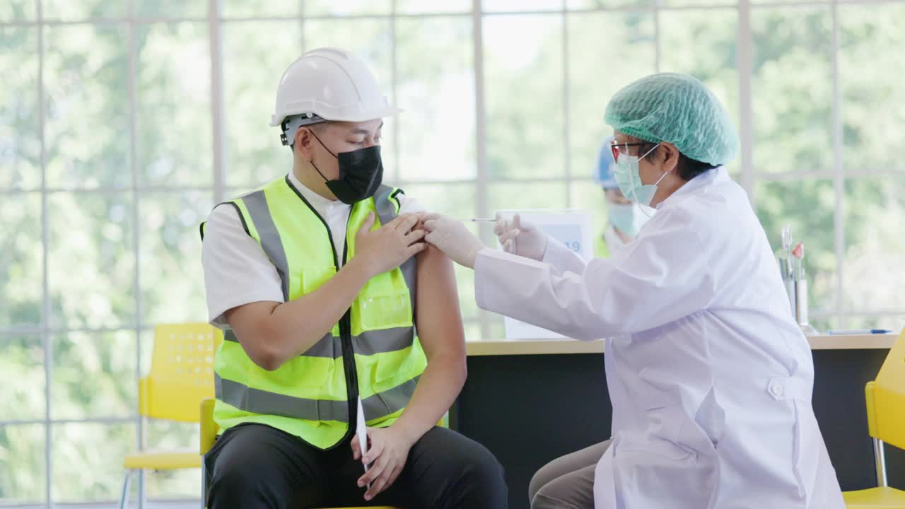 建筑行业新型冠状病毒疫苗接种站医生正在医院为团队工程工人接种疫苗，以保护COVID-19或流感。人们戴口罩以防御病毒。健康福利视频素材