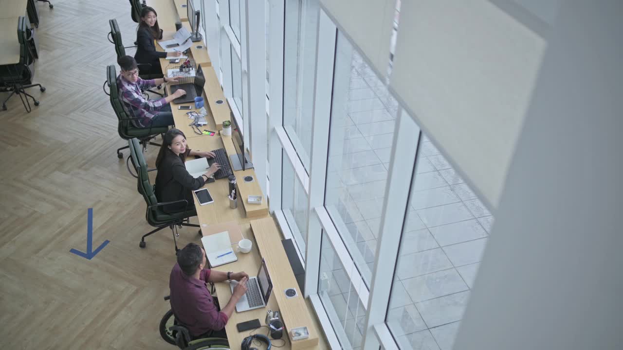 坐在轮椅上的印度商人正在创意办公室与他的中国女同事讨论视频素材