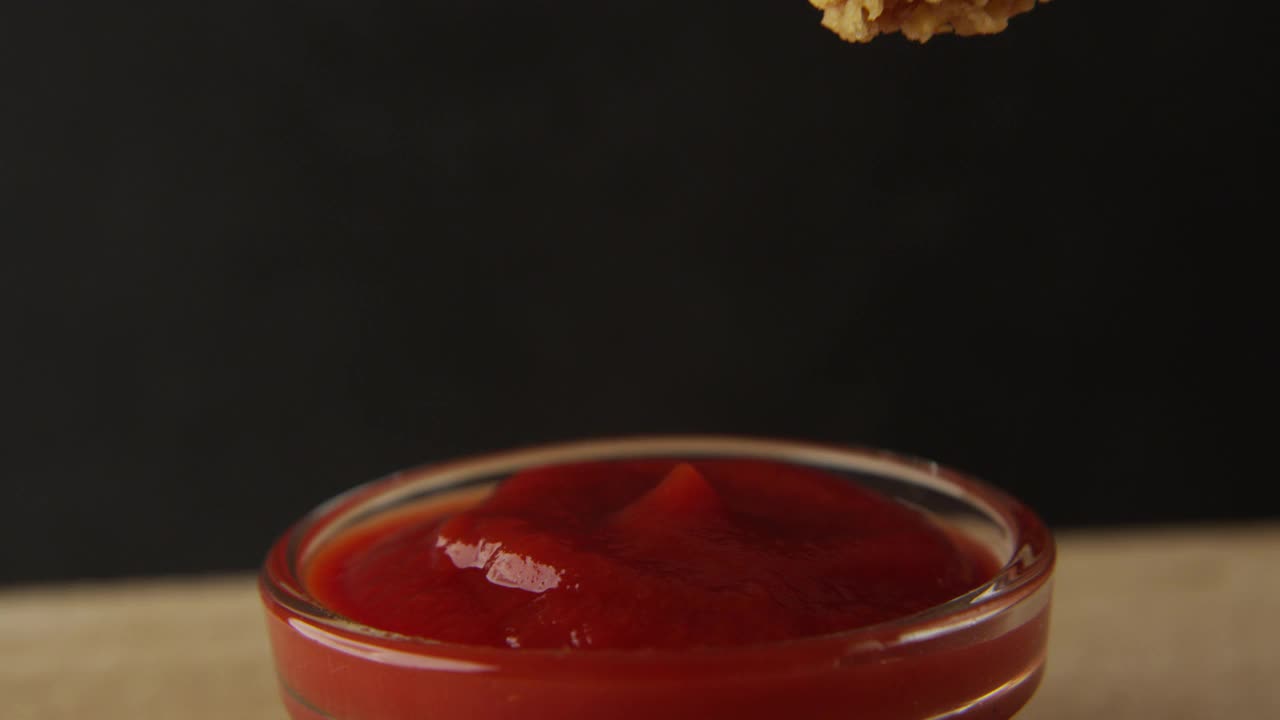 微距镜头:在黑色背景的桌子上，将鸡翅浸入番茄酱碗中视频素材