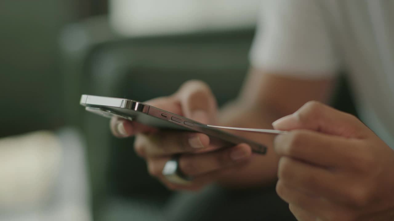 年轻的亚洲男人用她的手机用信用卡在网上订购视频下载