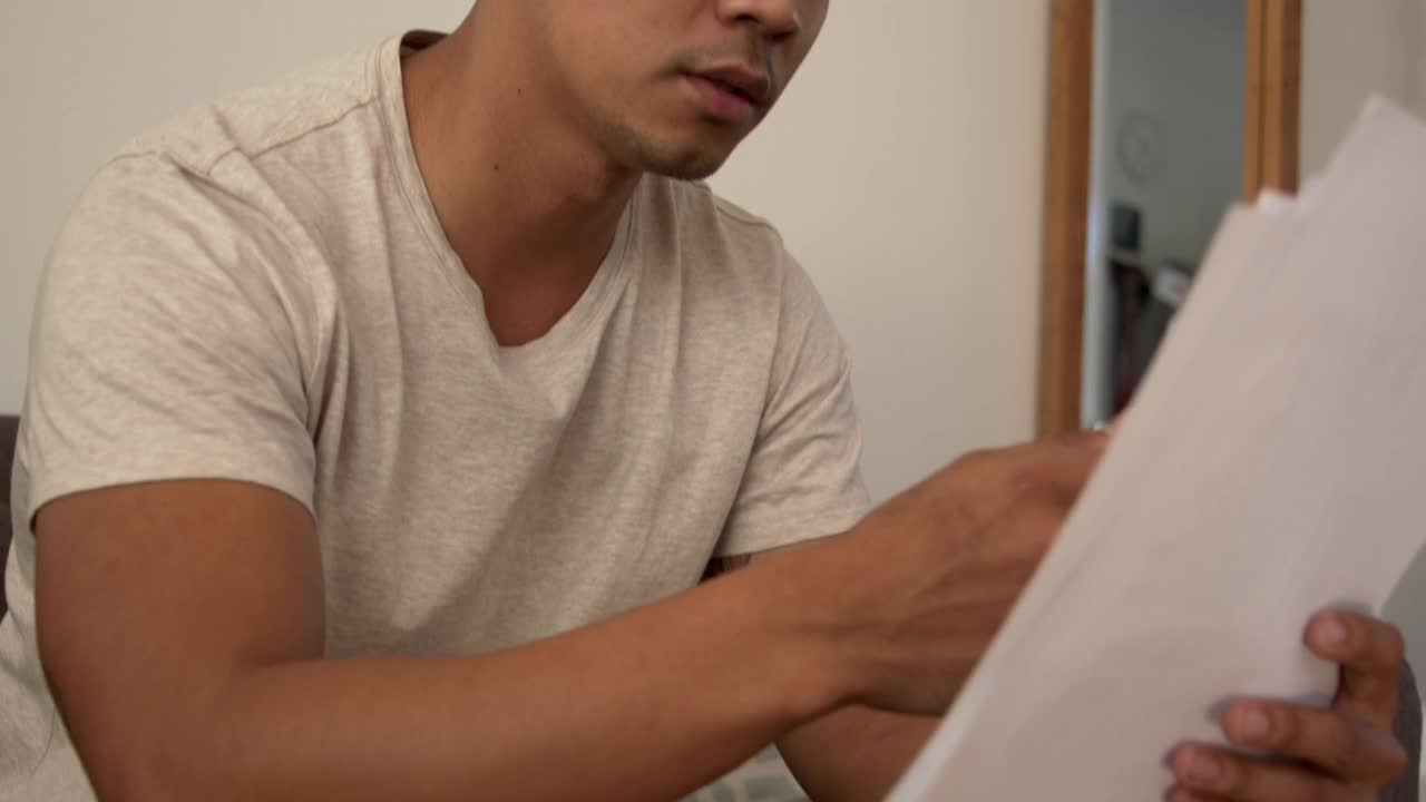 4k视频显示一个年轻人在家里处理文书工作时看起来很焦虑视频素材