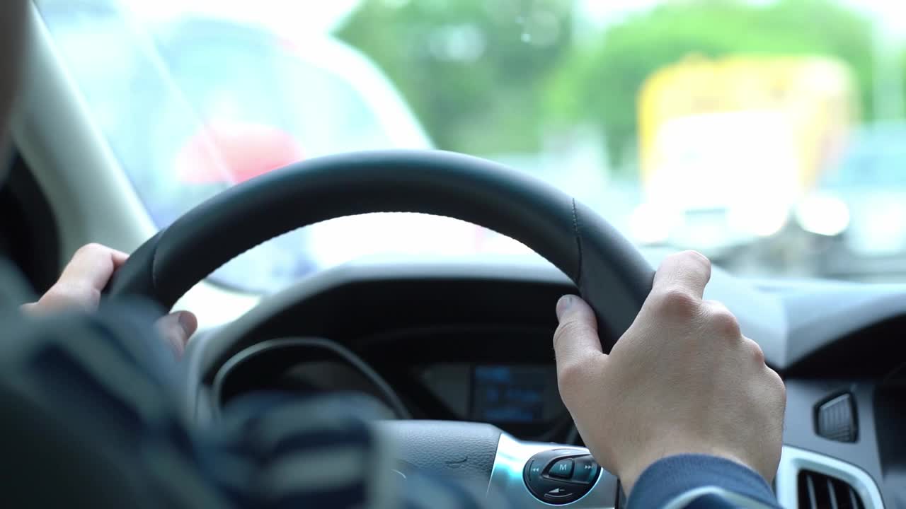 司机坐在方向盘后面，一名男子一边开车一边把手放在方向盘上，视频来自车内视频素材