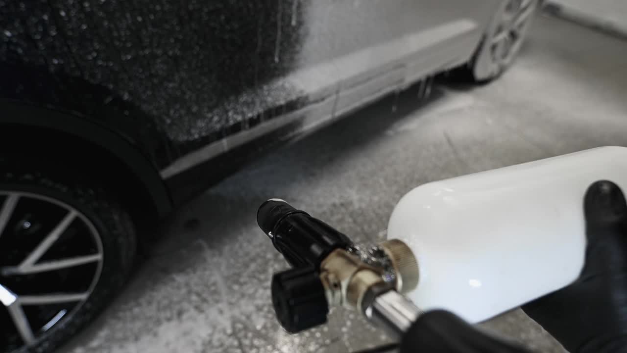汽车与站在洗车服务。POV:工人用高压喷雾器覆盖汽车泡沫视频素材