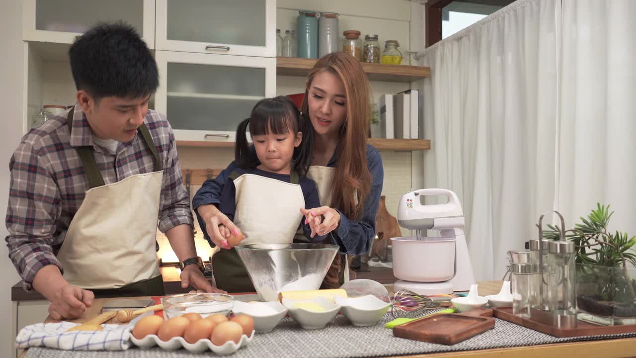 周末，亚洲父亲和母亲一起教日本女儿用手敲鸡蛋。亚洲家庭的概念，一个孩子做饭，烘焙，烘焙。十几岁的女孩有积极的情绪和兴奋去做。视频素材