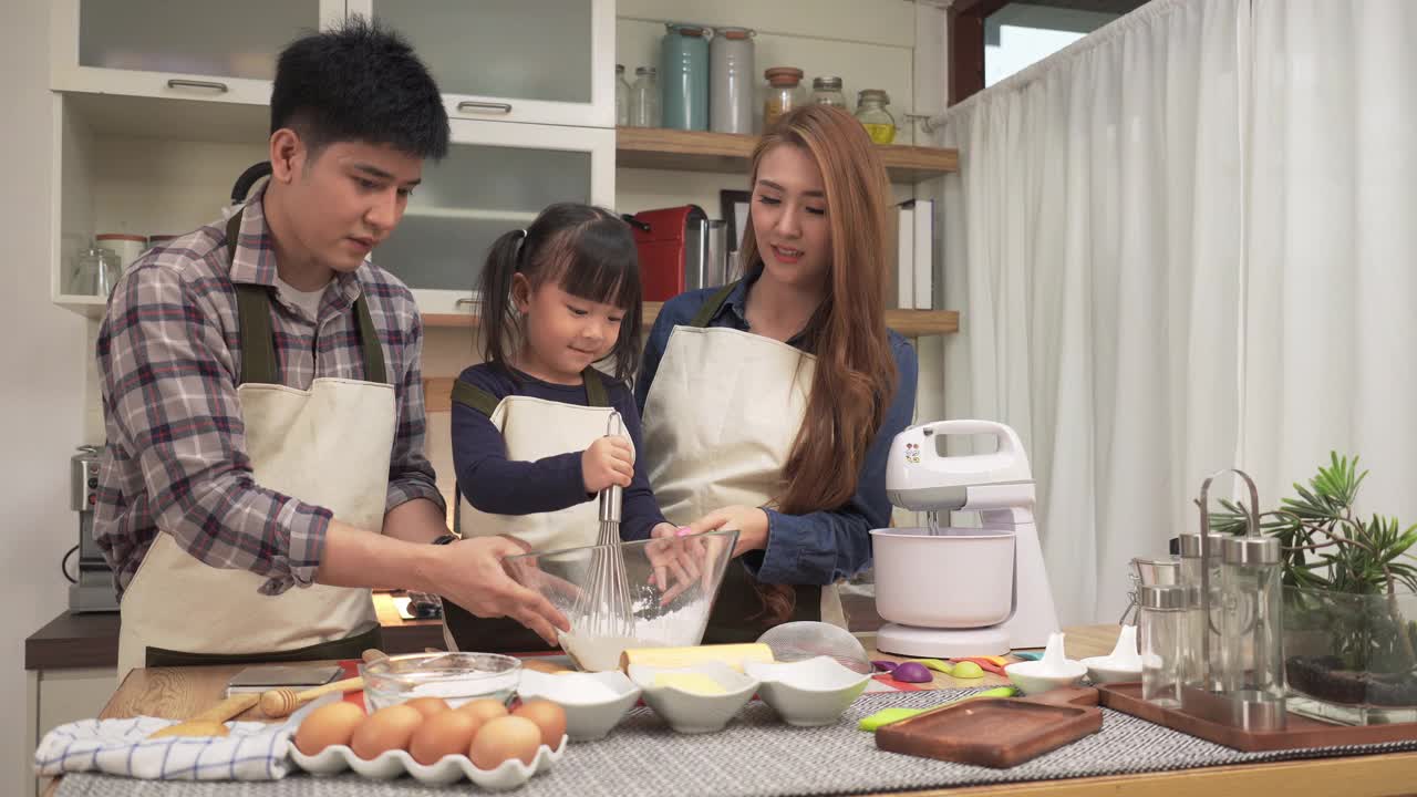亚洲父亲和母亲在周末教日本女儿用打蛋器打面团。亚洲家庭的概念，一个孩子做饭，烘焙，烘焙。十几岁的女孩有积极的情绪和兴奋去做。视频素材
