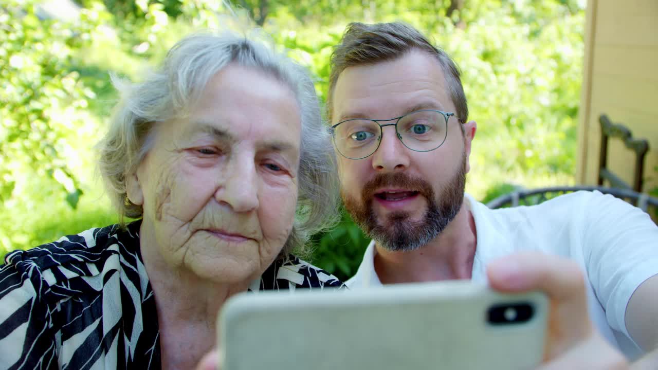 一名老妇人和一名成年男性亲属在视频通话，一名老妇露出两根手指，标志着战胜冠状病毒视频素材