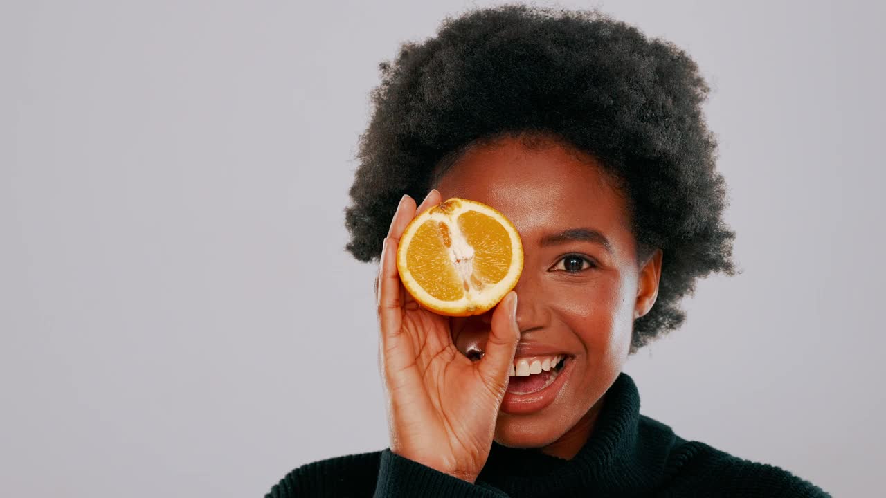 一段4k视频显示，一名年轻女子拿着半个橙子，在灰色背景下摆姿势视频下载