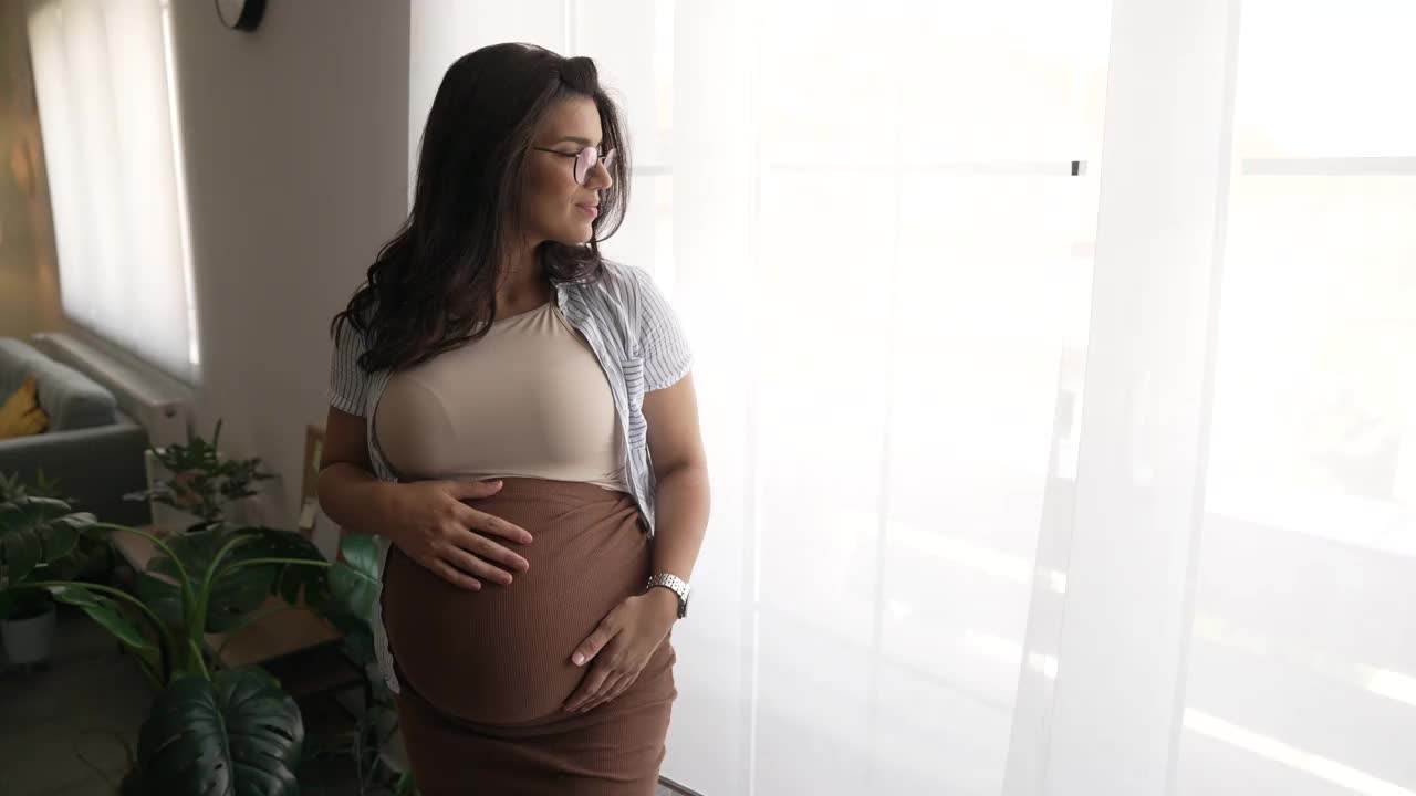 年轻快乐的孕妇站在窗边视频素材