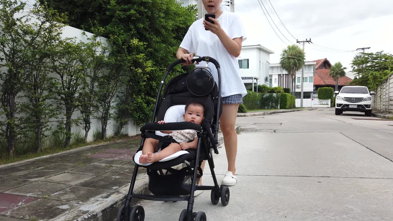 跟踪和广角亚洲成年母亲使用婴儿车与她的女儿和扬声器电话聊天的朋友在家里视频下载