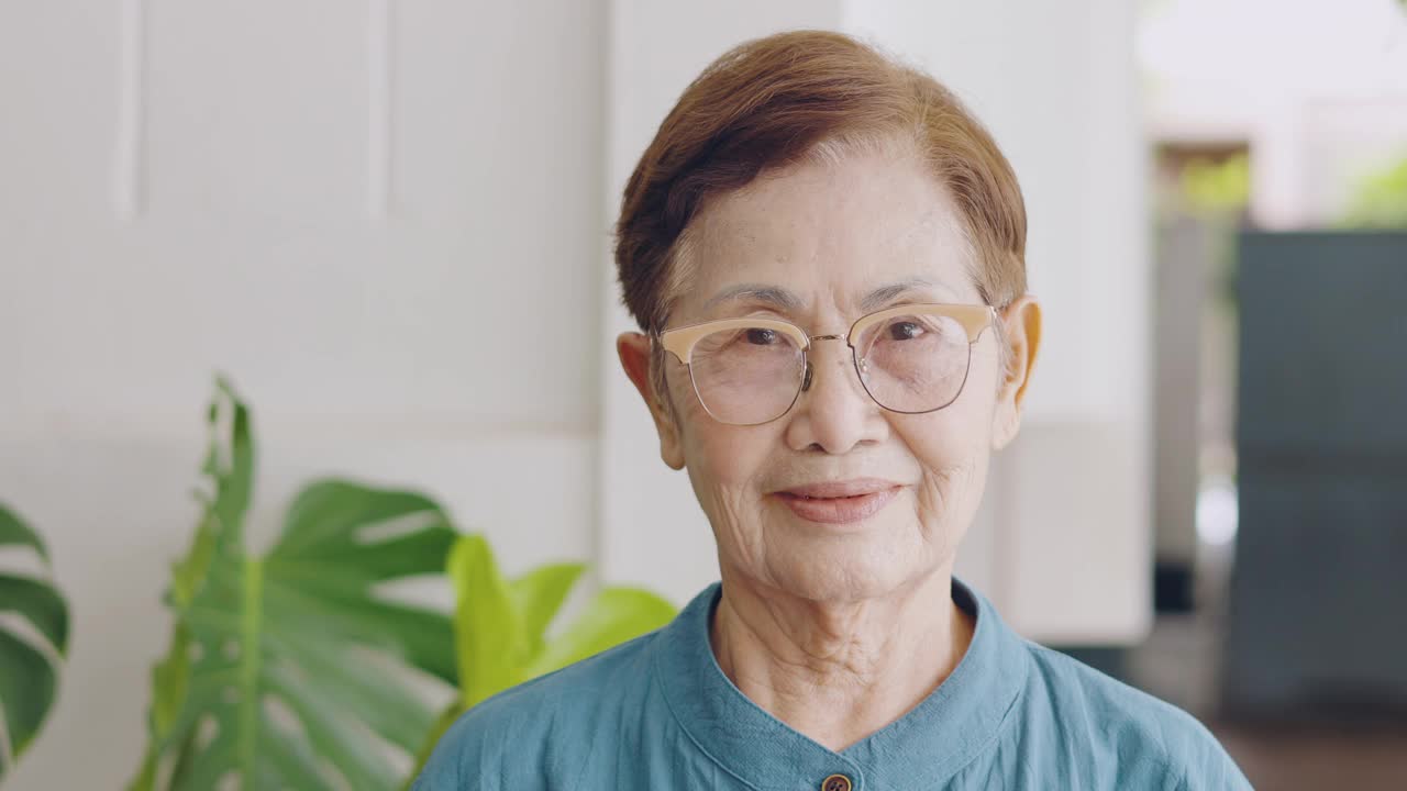 戴着眼镜的亚洲(泰国和中国)老奶奶的4K聚焦脸对着镜头微笑，对她幸福健康的退休生活表现出积极和享受。视频素材