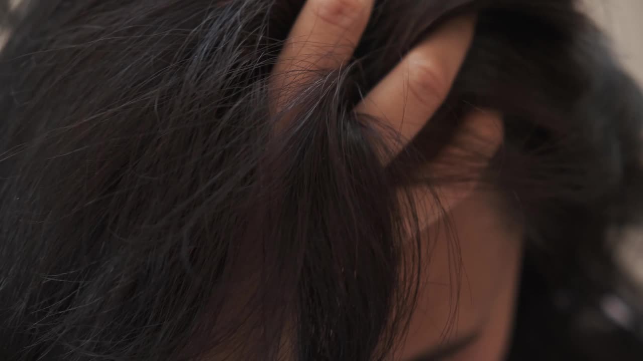 一位中年妇女抚摸着她乌黑的头发，头发的根部有一头灰白的头发视频素材