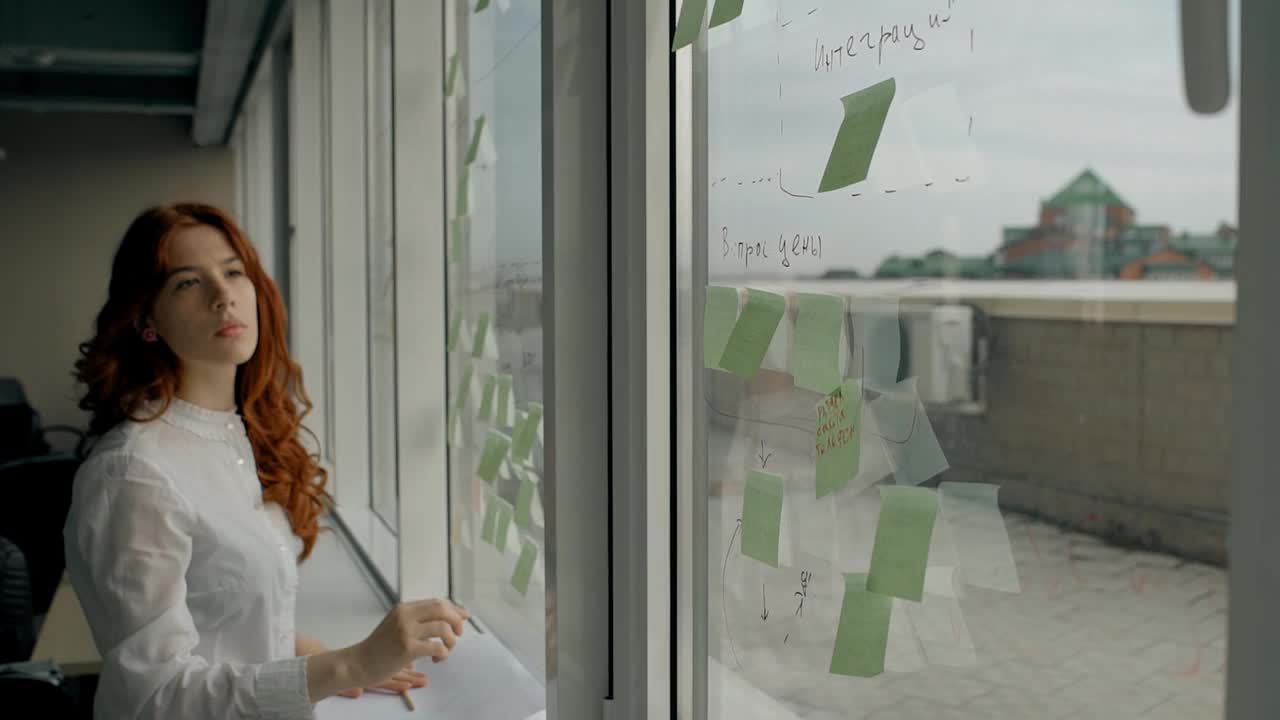 漂亮的年轻女人站在现代办公室的窗户上粘贴贴纸视频下载