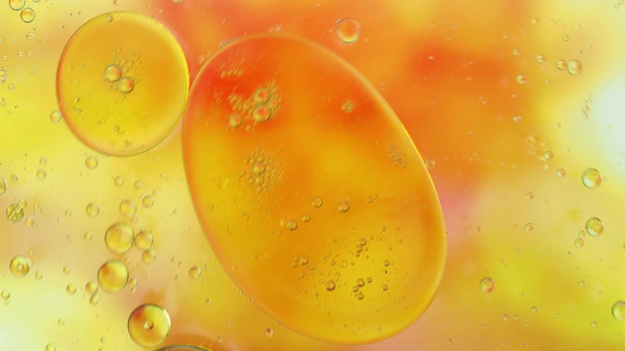 一个行星形状的液体气泡，漂浮在橙色液体的表面。视频素材