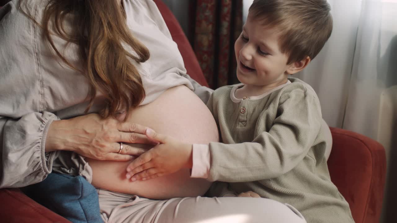 小男孩倾听着他怀孕的妈妈的肚子视频素材