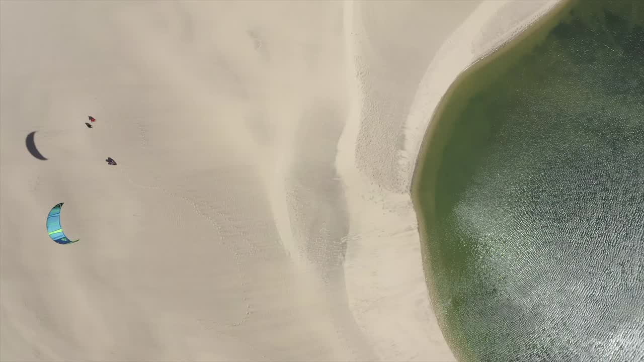 在沙滩附近的风筝板上，人们从沙丘上的无人机上风筝冲浪。——慢动作视频下载