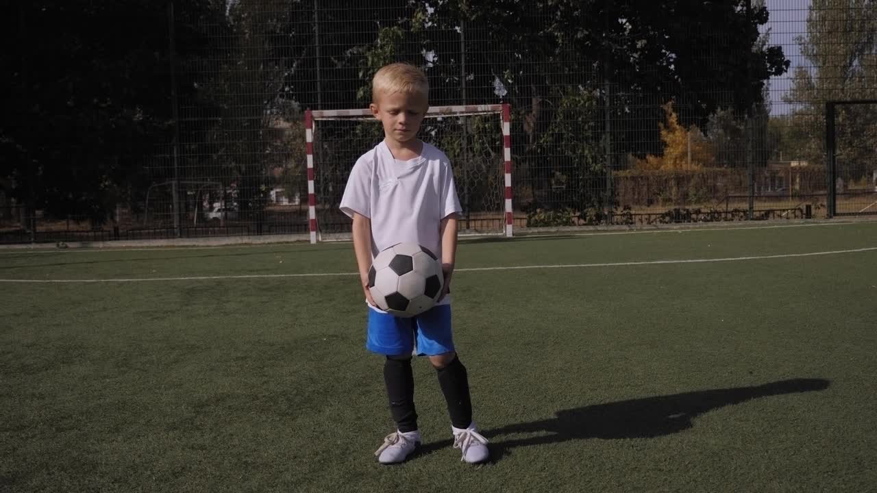 一个小男孩足球运动员在足球场上学习耍球。视频素材