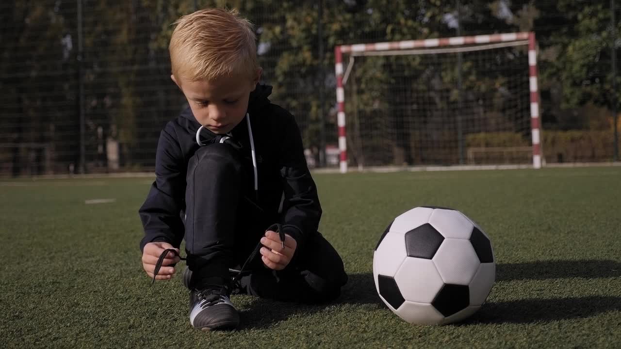 一个小男孩足球运动员在足球场上系鞋带。视频素材