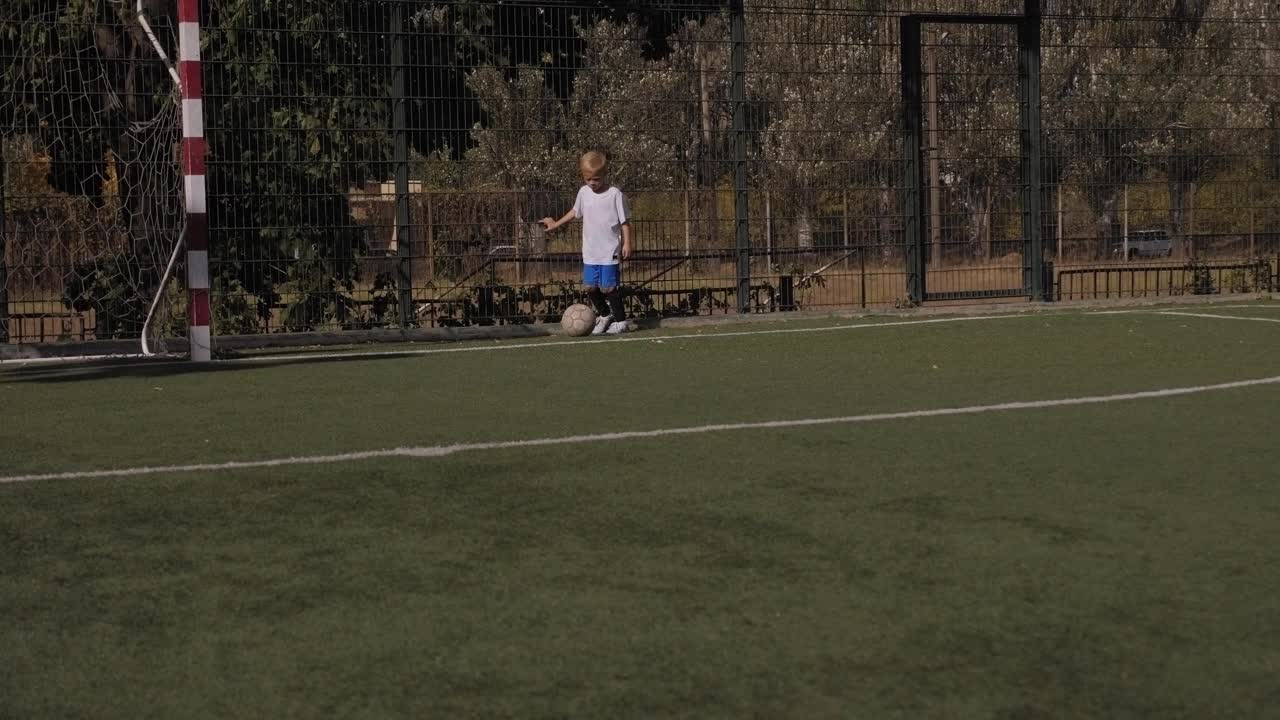一个小男孩在足球场上训练，练习运球和佯攻。视频素材