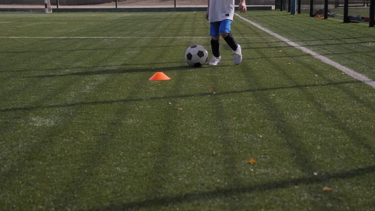 一个小男孩在足球场上训练，他练习带球和射门视频素材