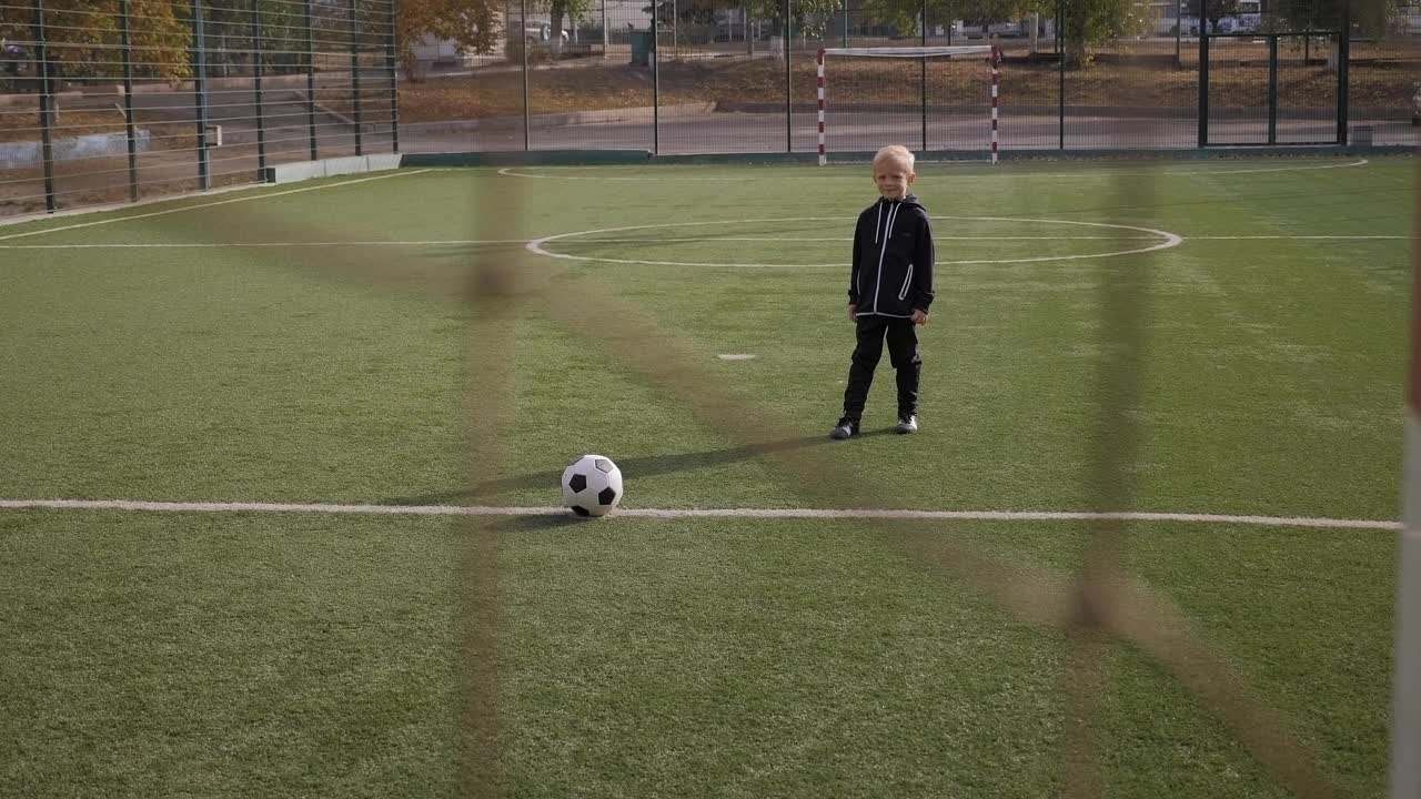 一个小男孩足球运动员用足球击中了球门。视频素材