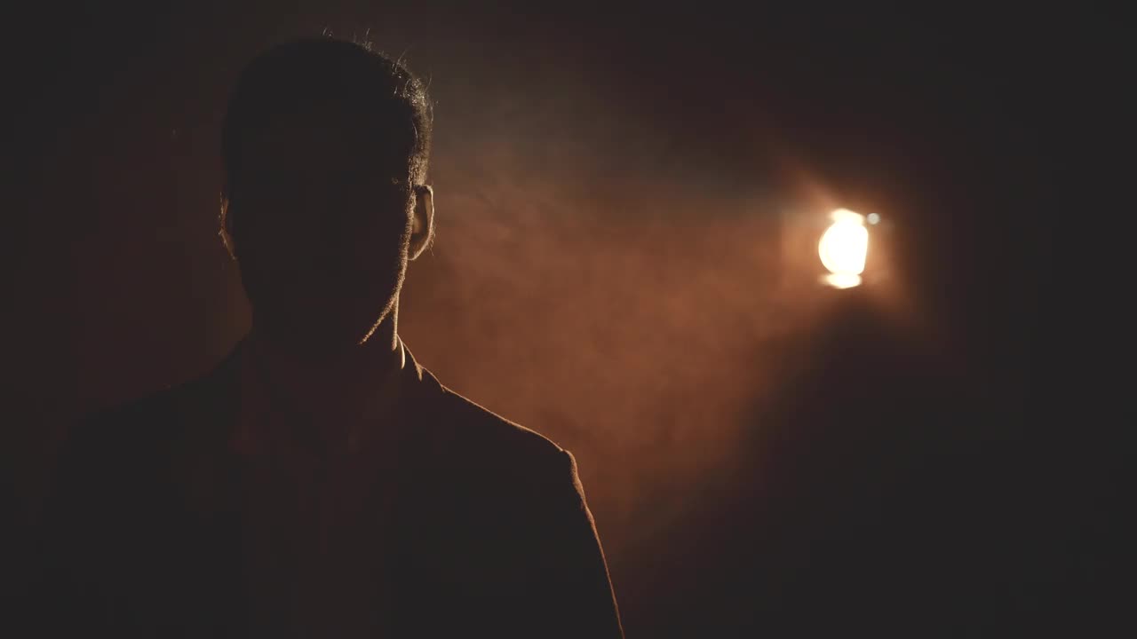 4k特写视频的男性的脸在阴影和烟雾在黑暗的背景。视频素材