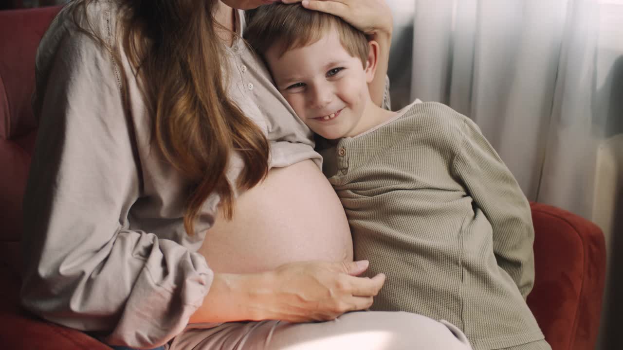 小男孩倾听着他怀孕的妈妈的肚子视频素材