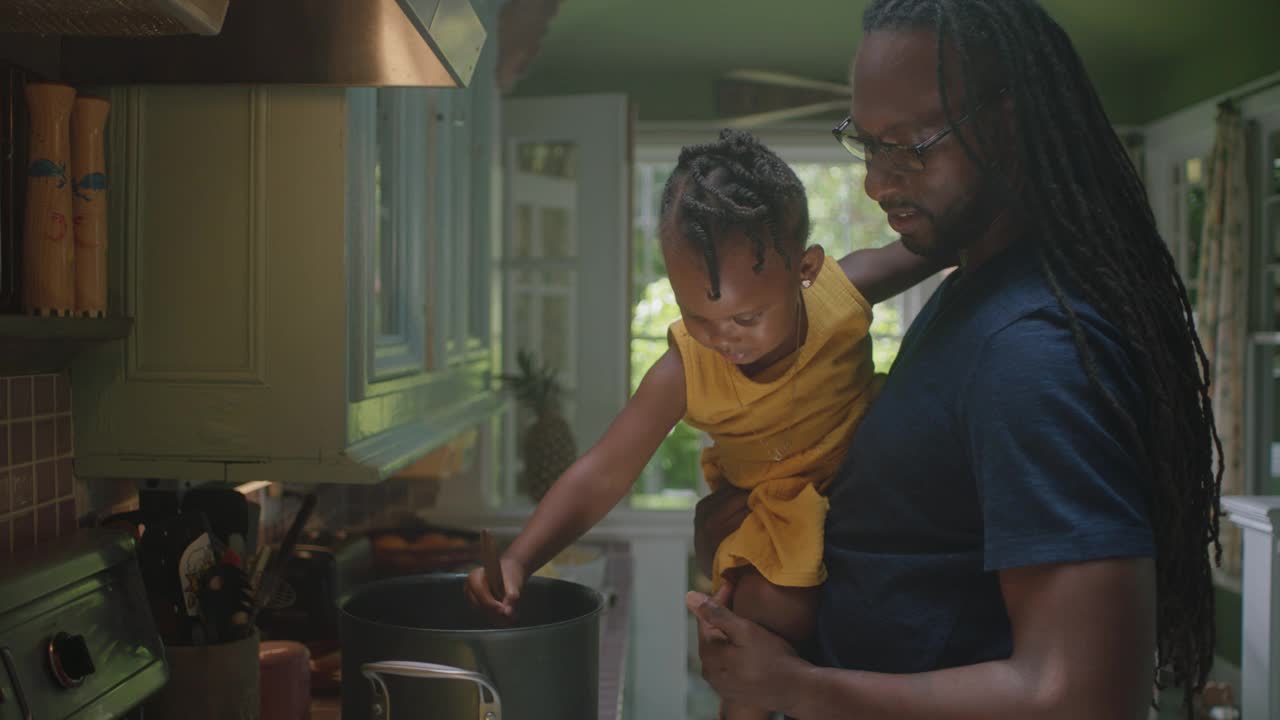 一个年轻人和一个小孩在厨房里搅拌锅里的情景视频下载