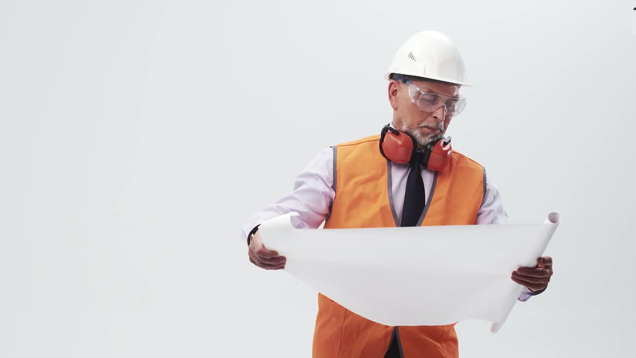 穿着制服的成年工程师研究工作图纸。在白色背景的工作室里，一个戴着头盔、穿着背心的建筑工看着施工方案视频素材