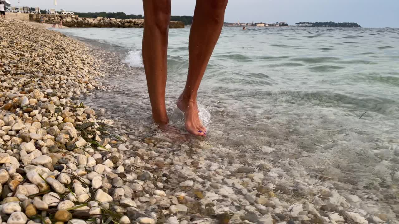 一个女人走在海边的鹅卵石上视频下载